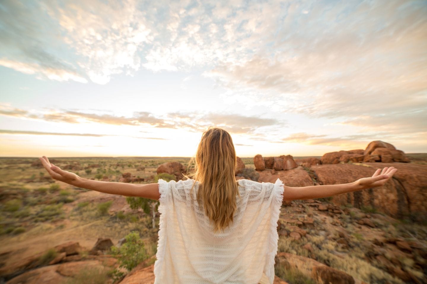 Person with outstretched arms facing a desert landscape during sunset.